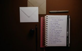 Overhead view of a to-do list notebook with New Year's resolutions, pens, and envelopes on a desk.