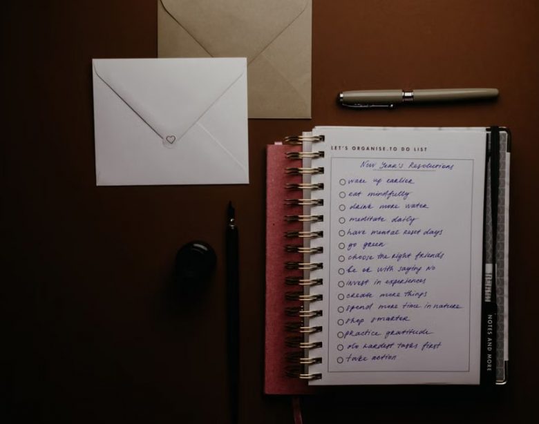 Overhead view of a to-do list notebook with New Year's resolutions, pens, and envelopes on a desk.